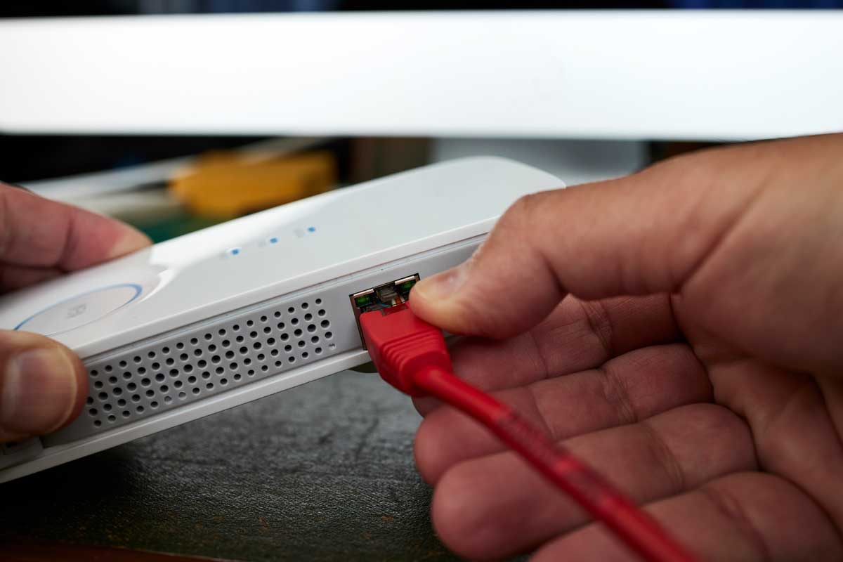 Mano che collega un cavo di rete rosso a un router, rappresentazione di installazione e gestione reti aziendali.
